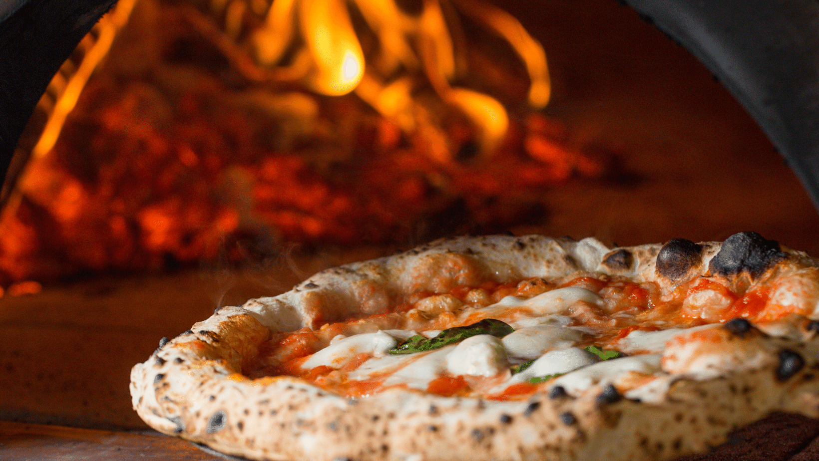 A Pizza Margherita sits in front of a fire in a fire pizza oven