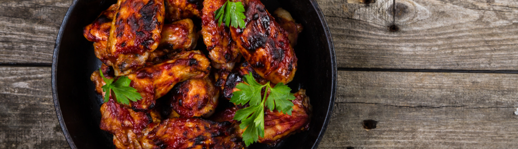 Cast iron pan with chicken baked inside on wood background