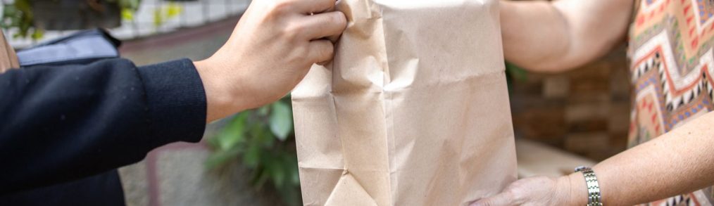 Delivery person handing brown bag over to customer outside home