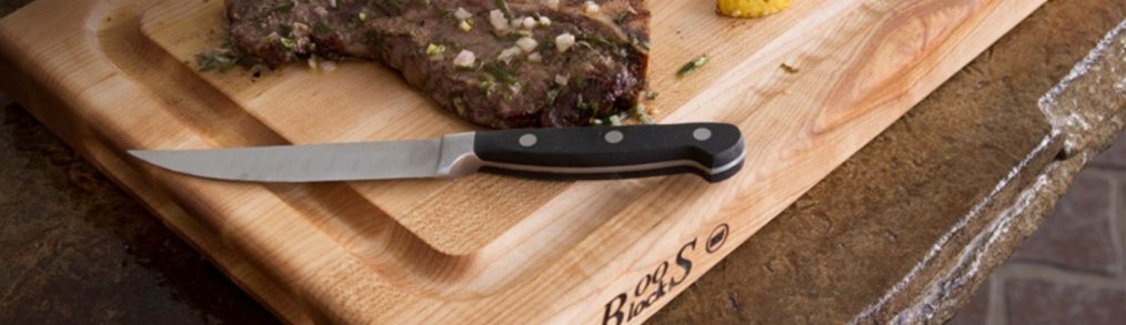 John Boos & Company wooden cutting board with black handled knife, steak, and slice on lemon on top