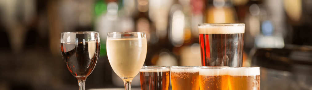 Glass of red wine, glass of white wine in front of flight of four sample beers that are in front of a pint of dark beer