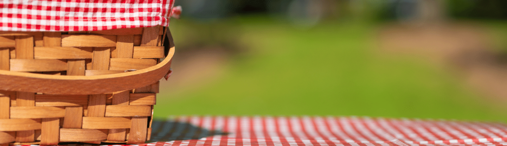 Picnic basket with red and white checked cloth inside sitting on top of table with red and white checker board tablecloth - summer celebrations