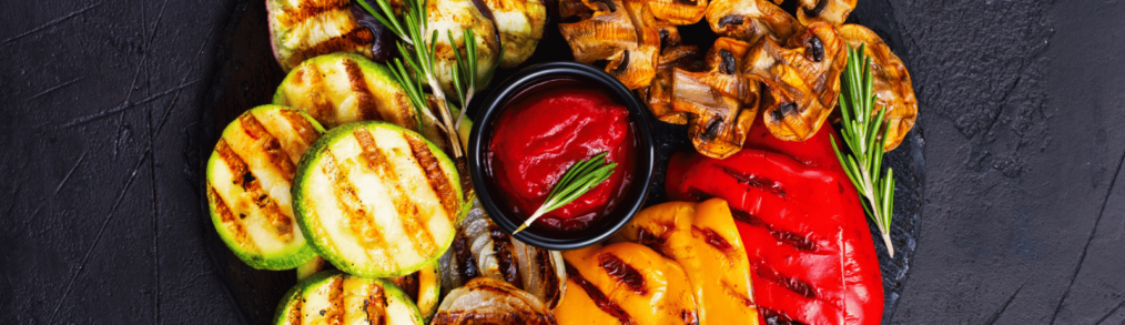 Platter of grilled charbroiling zucchini, red and yellow peppers, onions, eggplant and mushroom with red dipping sauce in the middle.