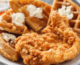 A white plate holds sliced Belgian waffles and a whole fried chicken breast. The slices of waffles are topped with whipped butter.
