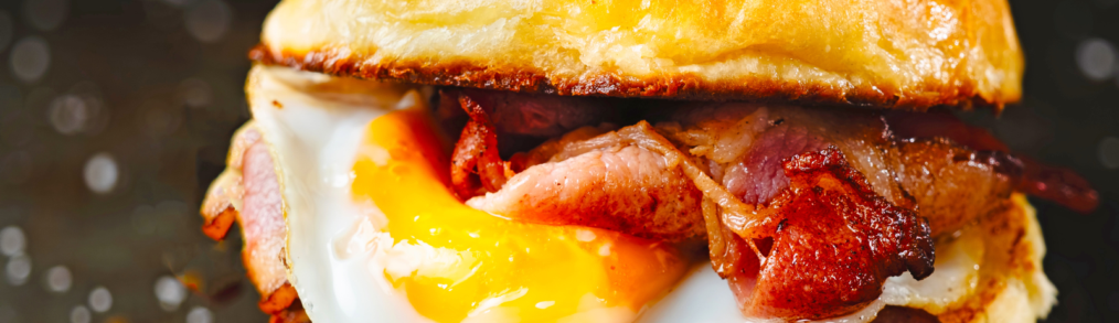 Breakfast sandwich with fried egg and bacon between brioche bun.