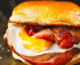 Breakfast sandwich with fried egg and bacon between brioche bun.