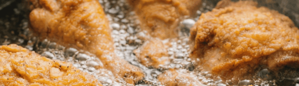 Multiple pieces of breaded fried chicken frying in bubbling oil in a commercial kitchen fryer
