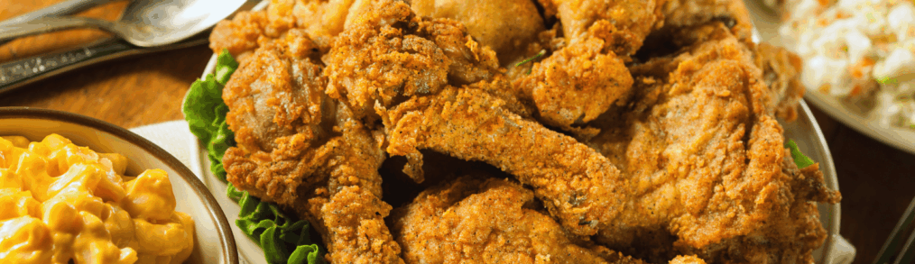 Platter of crispy fried chicken pieces served on a plate with macaroni and cheese and coleslaw on a restaurant table.