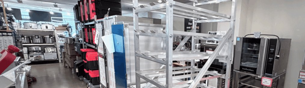 Alto-Hartley commercial kitchen equipment showroom in Alexandria, Virginia, featuring stainless steel bakery racks, convection ovens, prep tables, transport carts, and storage equipment used in restaurant and foodservice operations.