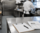 Commercial kitchen prep area with stainless steel surfaces and a clipboard — an operator reviews equipment specifications during commercial kitchen equipment selection