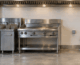 Nearly finished commercial kitchen cook line with an empty gap where an oven should be, showing a capped gas line and electrical box on the wall